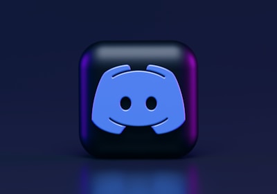 A 3D-style block with a blue logo in the center, set against a dark background. The logo resembles a game controller with two rounded edges and two circles on the front. The block has a subtle gradient, transitioning from dark to purple on its sides.